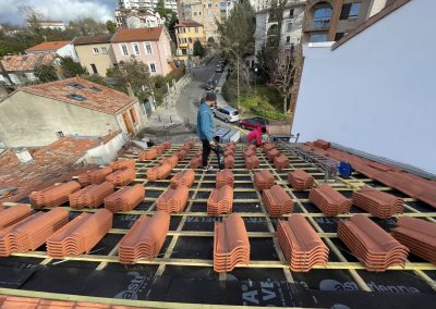 Travailleurs posant des tuiles en terre cuite sur toiture en construction.